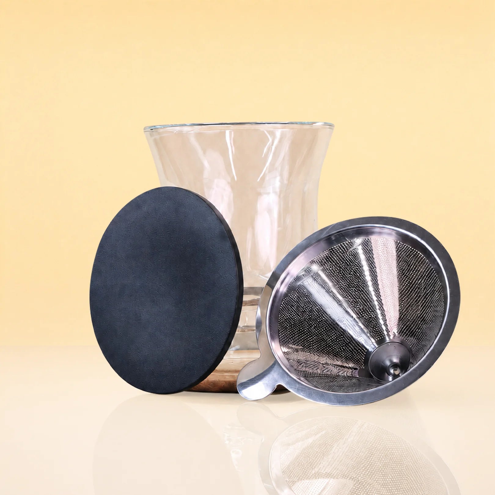 ObsidianEditionCeremonySet3 - A clear glass vase with a flared rim, shown with two accessories: a round black textured disc and a metal mesh funnel with a black rim, set against a warm beige background.