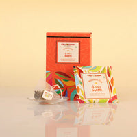 Chaai Choon Masala Chai 4 Spice Masti tea packaging, featuring a tall orange box with colorful leaf patterns, a single tea bag on a small clear saucer, and a single tea bag packet in front, set against a warm beige background.