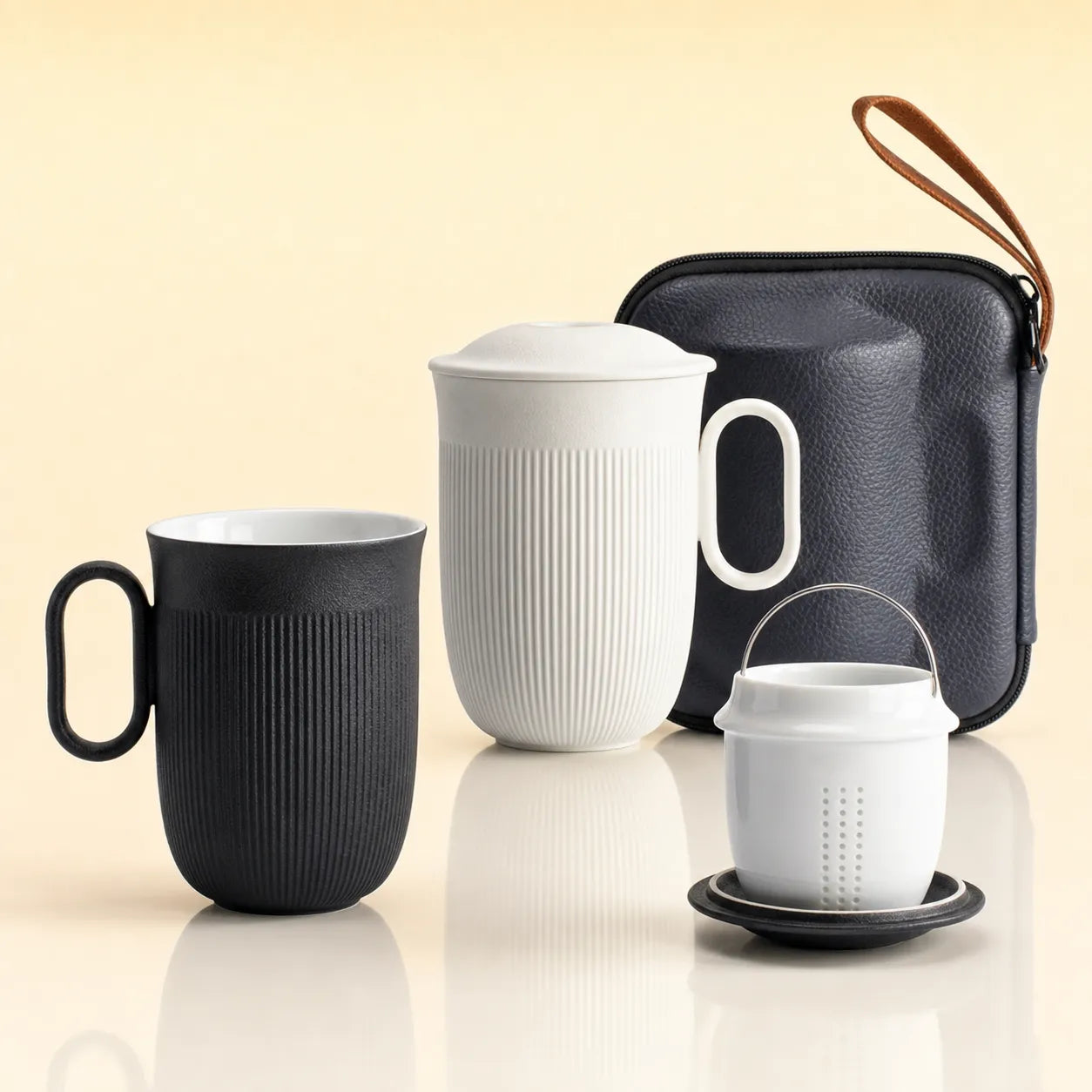 ChaiChun Infusion Mug - A set of four travel coffee accessories including a black ribbed handled mug, a white ribbed handled pitcher with lid, a white infuser filter cup on a saucer, and a black textured zippered carrying case with a brown wrist strap, arranged on a reflective light beige surface.