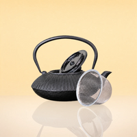 CharcoalInfusionFlutedIronTeapot2 - A black cast iron teapot with a ribbed textured body, a curved handle, a matching black lid, and a clear mesh strainer resting beside it on a reflective surface against a warm beige background.