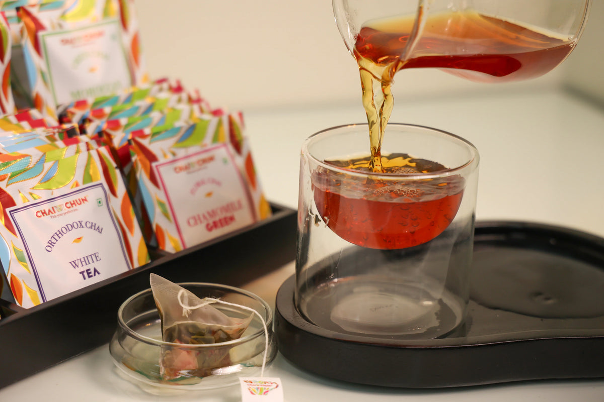 Conference & Banqueting - Tea bags from Oatly Crunch are displayed next to a glass teapot pouring amber tea into a clear glass cup on a black tray.