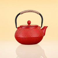 CrimsonBloomIronTeapot - A red textured cast iron teapot with a black handle wrapped in beige rope, shown on a reflective surface against a warm beige background.