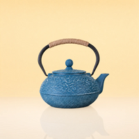IceVineIronTeapot - A blue cast iron teapot with a textured crackle pattern, featuring a black metal handle wrapped with natural brown twine, set against a warm beige background.
