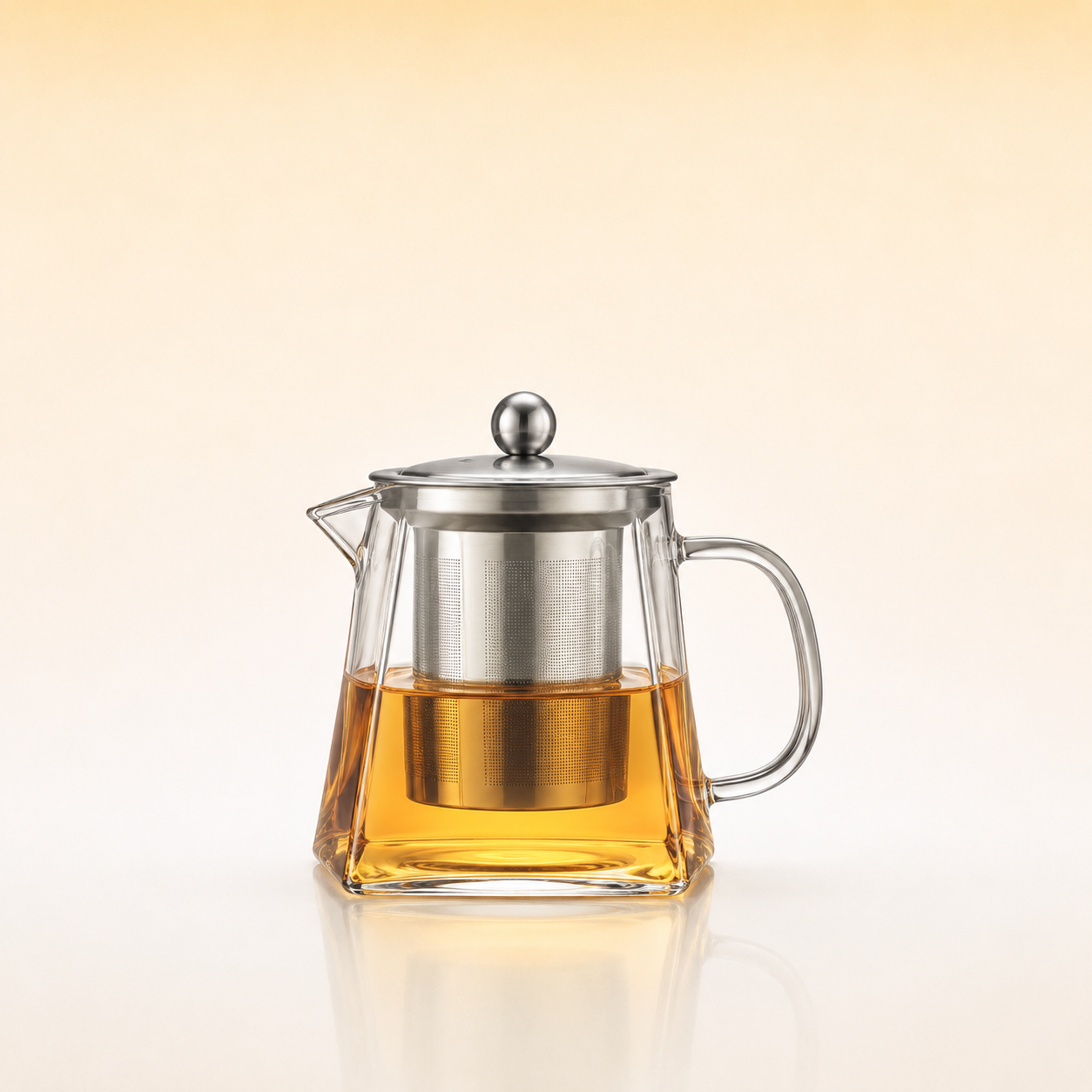 Infuser - A clear glass teapot with a stainless steel lid, metal infuser, and handle, filled with amber tea, centered on a warm beige gradient background with a soft reflection below.