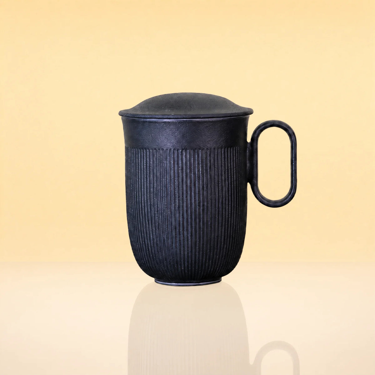 InfusionMug-CeramicTeaMugwithanInfuserandLid - A dark charcoal gray ribbed ceramic mug with a matching lid and a loop handle, shown on a reflective cream surface against a warm beige background.