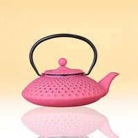 MagentaSteepIronTeapot - A pink perforated metal teapot with a black handle, shown on a warm beige gradient background with a soft reflection below.