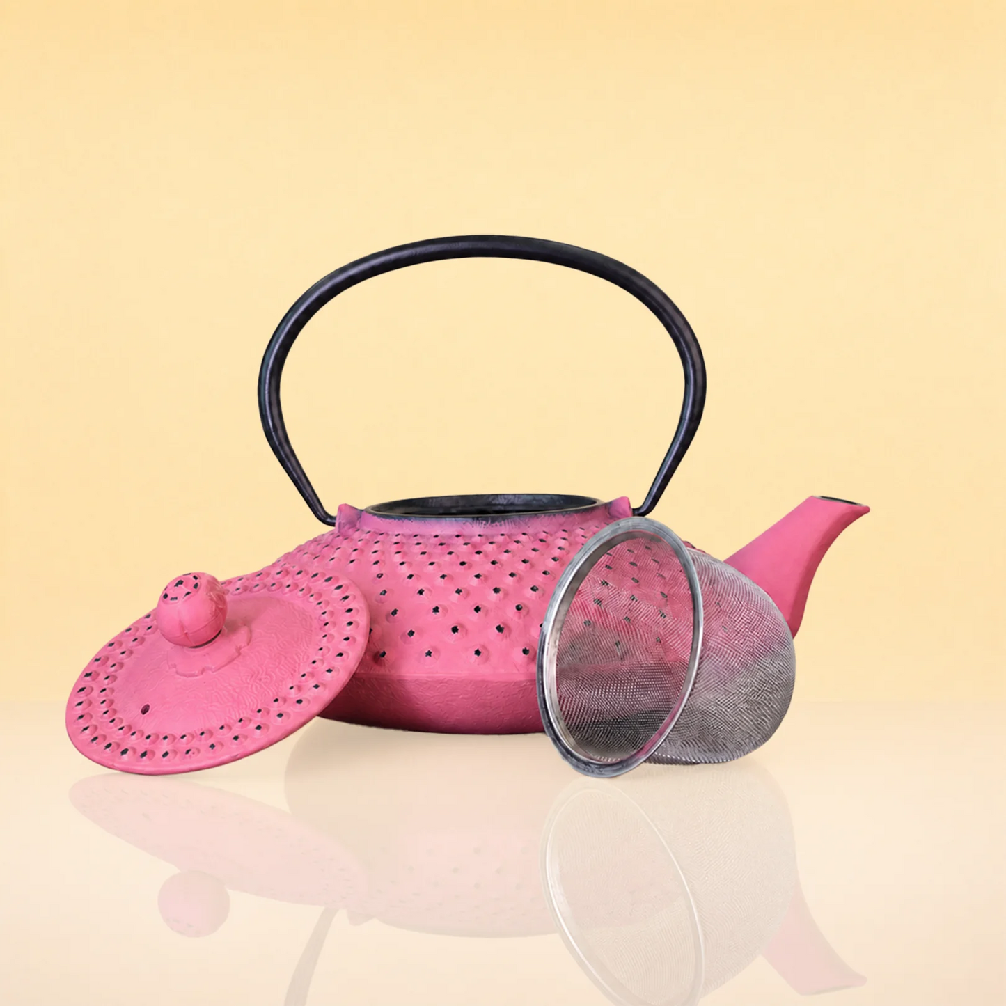 MagentaSteepIronTeapot2 - A pink perforated metal teapot with a black handle, shown with its matching pink lid and a silver mesh strainer on a reflective beige surface against a pale yellow background.