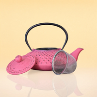 MagentaSteepIronTeapot2 - A pink perforated metal teapot with a black handle, shown with its matching pink lid and a silver mesh strainer on a reflective beige surface against a pale yellow background.