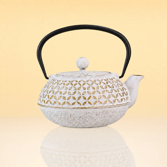 SageTerriorIronTeapot2 - A white cast iron teapot with a black handle and lid knob, featuring a decorative cutout pattern on the body, set against a warm beige gradient background.