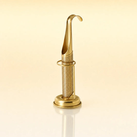 Signature Grip Infuser – Gold-toned stainless steel upright tea infuser with a hook-shaped handle, cylindrical mesh body, and a circular base stand, photographed on a warm cream background with a soft reflection below.