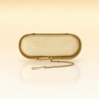 Silk Oval Infuser – Gold-toned stainless steel oval-shaped tea infuser with a hinged lid, rounded edges, and a delicate gold chain with clasp, photographed on a warm cream background with a soft reflection below.