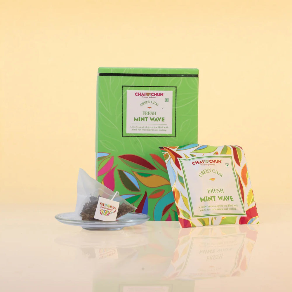 fresh-mint-wave - A box and individual packet of Chaji Chai Green Chai Fresh Mint Wave tea bags on a reflective surface against a warm beige background.