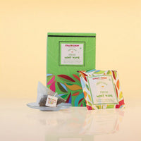 fresh-mint-wave - A box and individual packet of Chaji Chai Green Chai Fresh Mint Wave tea bags on a reflective surface against a warm beige background.
