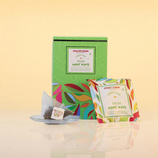 fresh-mint-wave - A box and individual packet of Chaji Chai Green Chai Fresh Mint Wave tea bags on a reflective surface against a warm beige background.