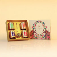 maharaja-collection-vol-2 - A boxed tea gift set displayed on a warm cream background. The open gold-toned box contains four small labeled tea tins and a metal tea infuser, with the illustrated outer box standing beside it.